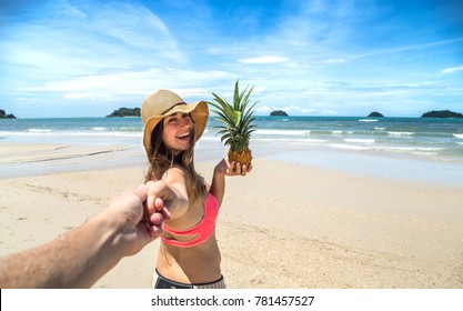beautiful girl in swimsuit and pineapple walks on the beach holding the hand of the guy, a romantic walk