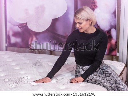 Beautiful girl touches the mattress. She examines the mattress she wants to buy. Testing how soft
