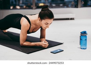 Beautiful girl training in the gym. Young woman performs an abdominal plank while checking the run on the smartphone. Russian classic dancer doing stretching and yoga poses - Powered by Shutterstock