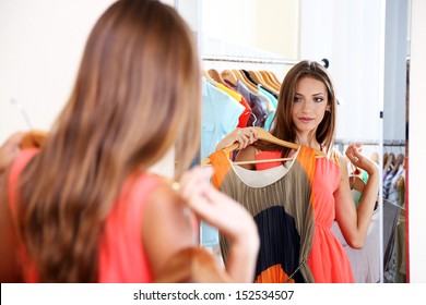 Beautiful Girl Trying Dress Near Mirror On Room Background