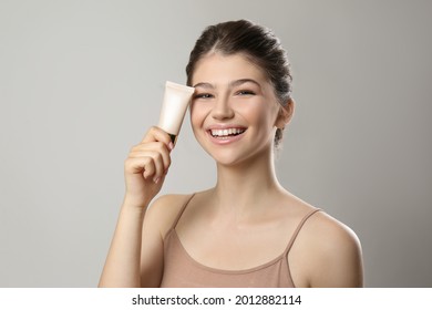 Beautiful girl with tube of foundation on light grey background