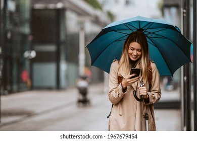 Beautiful girl with an umbrella standing in the rain typing a message. - Powered by Shutterstock