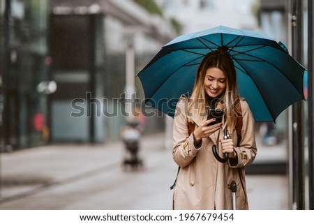 Beautiful girl with an umbrella standing in the rain typing a message.