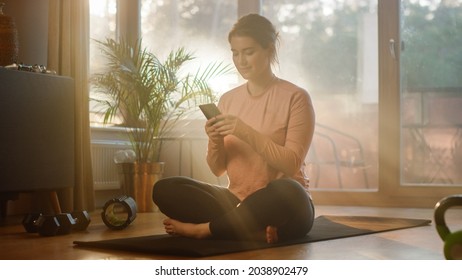 Beautiful Girl Using Smartphone After Fitness Workout At Home. Determined Plus Size Woman Using Fitness Tracker, Yoga Exercises Application, Browsing Online Health Articles, Posting On Internet