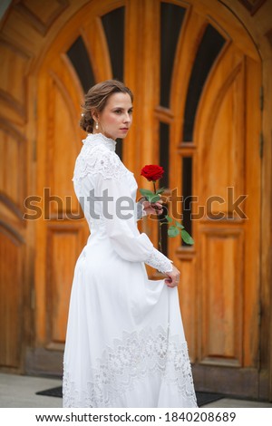 beautiful girl in a vintage dress walks in the garden, bride with a red rose in her hands
