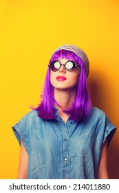 Beautiful girl with violet hair in sunglasses on yellow background.