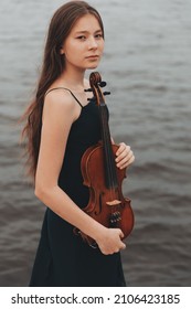a beautiful girl with a violin stands against the background of water. Asian appearance. musical concept. High quality photo