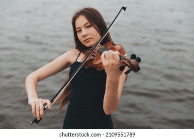 a beautiful girl with a violin stands against the background of water. Asian appearance. musical concept. High quality photo