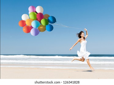 Beautiful girl walking in the beach while holding colored balloons - Powered by Shutterstock