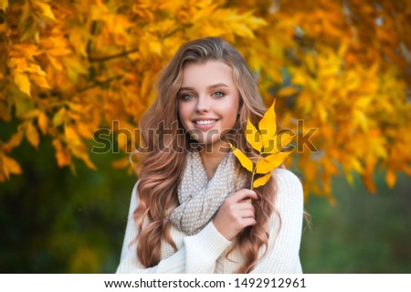 Beautiful girl walking outdoors in autumn. Smiling girl collects yellow leaves in autumn. Young woman enjoying autumn weather.