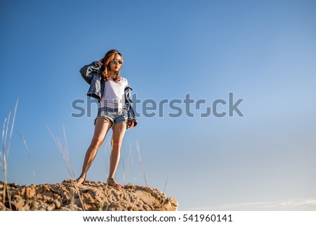 a beautiful girl wearing blue jean jacket standing on the cliff with blue sky background.