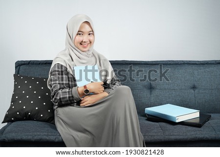 Beautiful girl wearing hijab sitting on a blue sofa with a blank book.