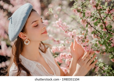 Beautiful girl wearing stylish blue beret, pearl earrings, posing near blooming sakura flowers. Model closed eyes. Spring, fashion, beauty, lifestyle conception. Copy, empty space for text