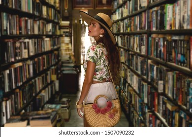 Beautiful girl wearing stylish outfit looking for interesting book in the small vintage bookstore  - Powered by Shutterstock