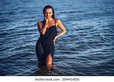 Beautiful Girl In Wet Black Dress Posing In Water. Fashion Colors, Glamour Portrait Of Pretty Beautiful Fashion Woman In Summer In Sea, Tropic Island Girl, Beautiful Tan, Skin Care And Pretty Face. 