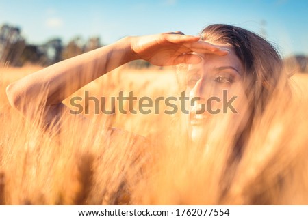 Similar – Junge Frau bedeckt ihr Gesicht vor der Sonne auf einem grünen Feld.