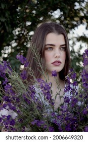 Beautiful girl in white dress holding a bouquet of purple flowers in field. Concept of natural and vintage look. A young girl in love. Long natural brown hair, very soft makeup.