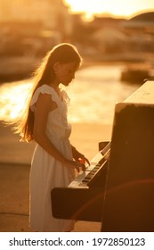Beautiful girl in a white dress plays the piano on the pier by the sea at sunset