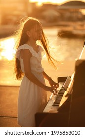 Beautiful girl in a white dress plays the piano on the pier by the sea at sunset