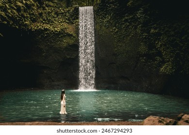 Beautiful girl in white dress posing and admiring the amazing Tibumana Waterfall in Bali, considered one of the best waterfalls in Bali - Powered by Shutterstock