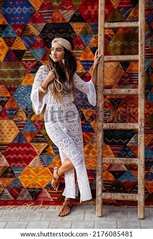 A beautiful girl in a white dress stands near a Moroccan carpet. Essaouira. Morocco