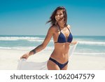 Beautiful girl with white fabric walking on the beach. Happy young woman relaxing at the beach and holding white scarf at wind in summer vacation. Latin tanned woman in blue bikini.