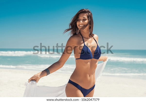 海岸を歩く白い布を着た美しい女の子 夏休みに ビーチでくつろぎ 風で白いスカーフを持つ幸せな若い女性 青いビキニの中のラテン色の女性 の写真素材 今すぐ編集