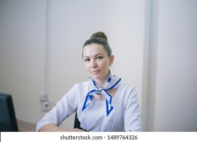 Beautiful Girl In A White Shirt And With A Scarf Around Her Neck Sits In The Office At The Computer And Types On The Keyboard