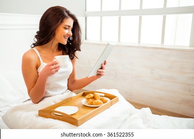 Beautiful girl in a white shirt using a tablet during breakfast in bed - Powered by Shutterstock