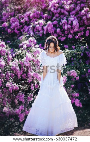 Beautiful girl in white vintage dress posing near bushes of a lilac