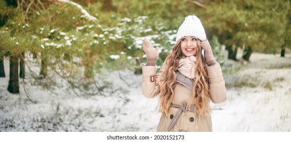 A Beautiful Girl In The Winter Forest Talks On The Phone And Smiles. The Blonde In A White Hat And Beige Coat Does Not Look At The Camera. Concept - Christmas, Sale. A Place For Text. Banner