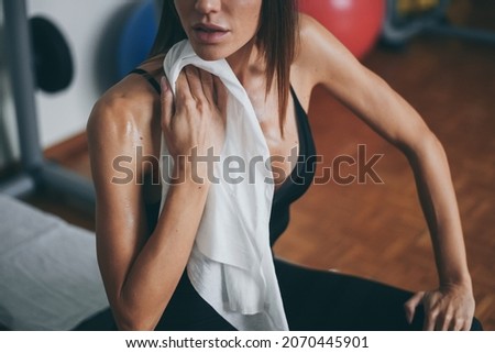 Beautiful girl wipes the sweat after training session. Young sporty woman at the end of the session in the gym. Sweaty athlete with towel ready to take shower. Sport, health, youth and leisure concept