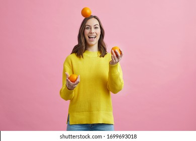 Beautiful girl, woman and person juggleling with fruit, oranges and lemon on a contrastfull colored pink background. Concept: gestures with frugt with colors.