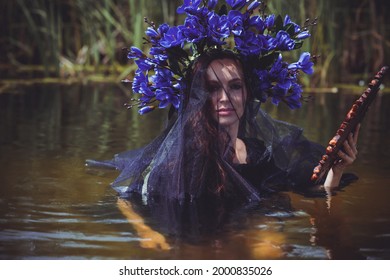 Beautiful girl in wreath of flowers at lake. Portrait of Young beautiful woman. Young pagan girl conduct ceremony on Midsummer. Earth Day