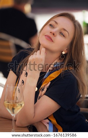 
beautiful girl with a yellow scarf on her neck and a glass of wine is sitting in a restaurant