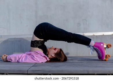 Beautiful Girl In Yoga Pose Lying On Her Back With Her Legs Over Her Head On Roller Skates In The Park