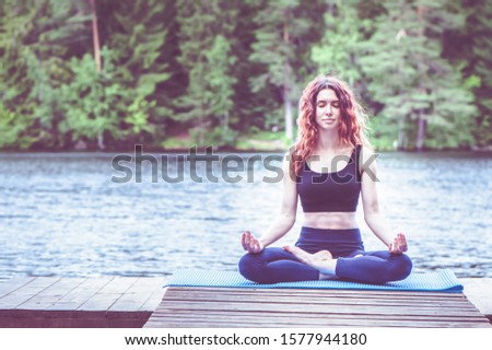 Beautiful girl in a yoga pose on the lake. Lotus position , Padmasana. The concept of appeasement,  healthy lifestyle. Space for text