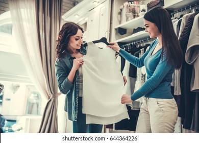 Beautiful Girls Are Choosing Clothes, Talking And Smiling While Doing Shopping In Boutique