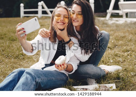 Beautiful girls in a park. Friends have fun in a summer park. Ladies sitting on the grass with a donuts