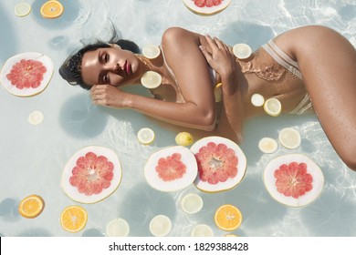 Beautiful Girl's Portrait In Water With Floating Slices Of Grapefruit And Citrus. Woman With Perfect Slim Body In Bikini Posing In Pool At SPA.