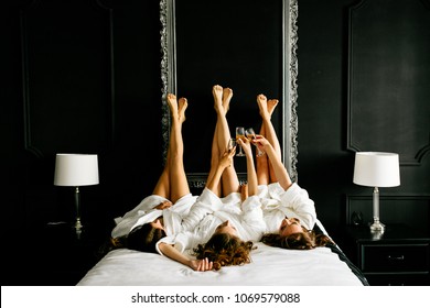 Beautiful girls raised their legs up and clink champagne glasses lying on the bed