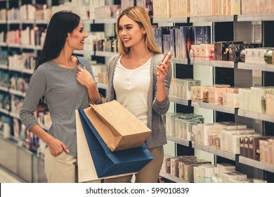 Beautiful girls with shopping bags are choosing perfumes and smiling while doing shopping in the mall