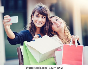 Beautiful girls with shopping bags taking a "selfie" with their cell phone - Powered by Shutterstock