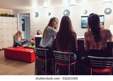 Beautiful Girls Sitting At The Bar In Hostel, Watching Tv And Talk.