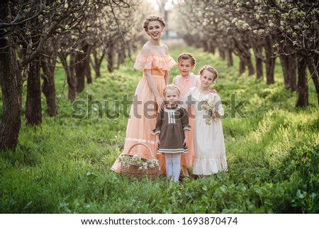 beautiful girls and their older sister for a walk in the flowered garden. The idea and concept of a friendly family and a happy childhood. Retro dresses