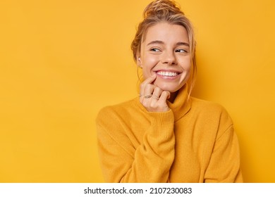 Beautiful glad woman smiles tenderly looks away with happy expression thinks about pleasant things wears casual soft jumper isolated over yellow background blank copy space for your promotion - Shutterstock ID 2107230083