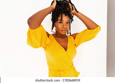 Beautiful glamorous black young woman fashion model in trendy summer yellow beauty dress straightens modern stylish dreadlocks hairstyle on white background in studio.