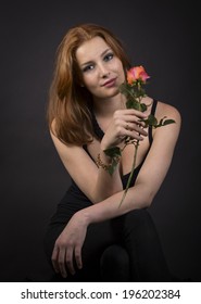 Beautiful glamorous woman in a stylish black outfit with shoulder length brown hair holding a single long stemmed rose as she smiles gently at the camera dreaming of her sweetheart or Valentine.