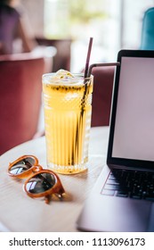 Beautiful Glass Of Yellow Passionfruit Lemonade, Trendy Sunglasses And Laptop On The Wooden Table. Flatlay Style, Spotted On The City Cafe.