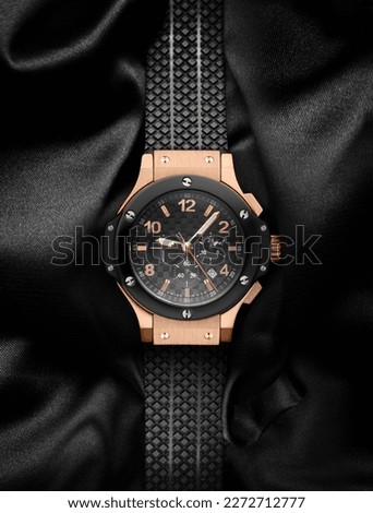 A beautiful gold men's watch with a black strap on a beautiful background made of textile or other black material. Beautiful gold watch. Branded luxury watch